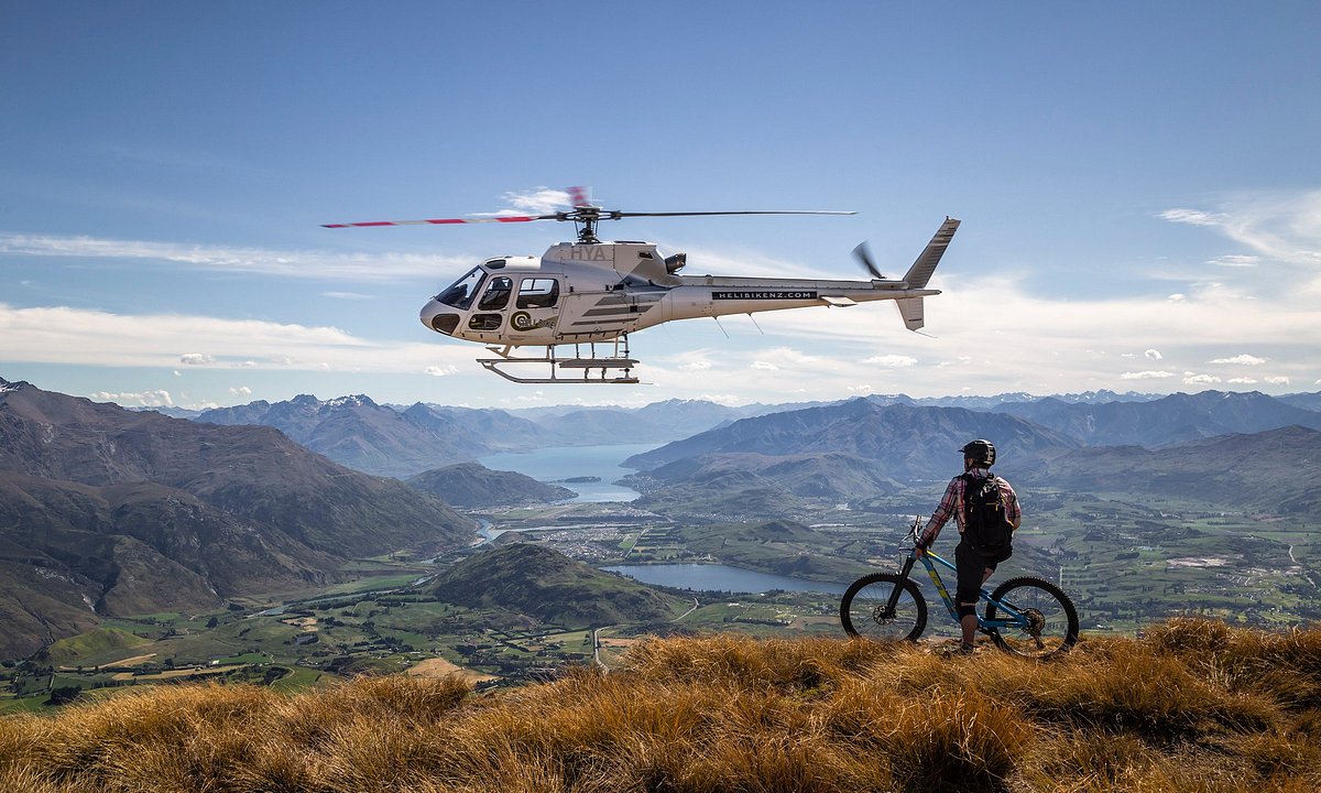 HelibikeNZ helicopter hovering beside a rider on a tussock summit